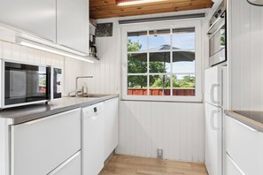 Cocina con alacenas blancas, microondas, lavavajillas y ventana con vista a zonas verdes.