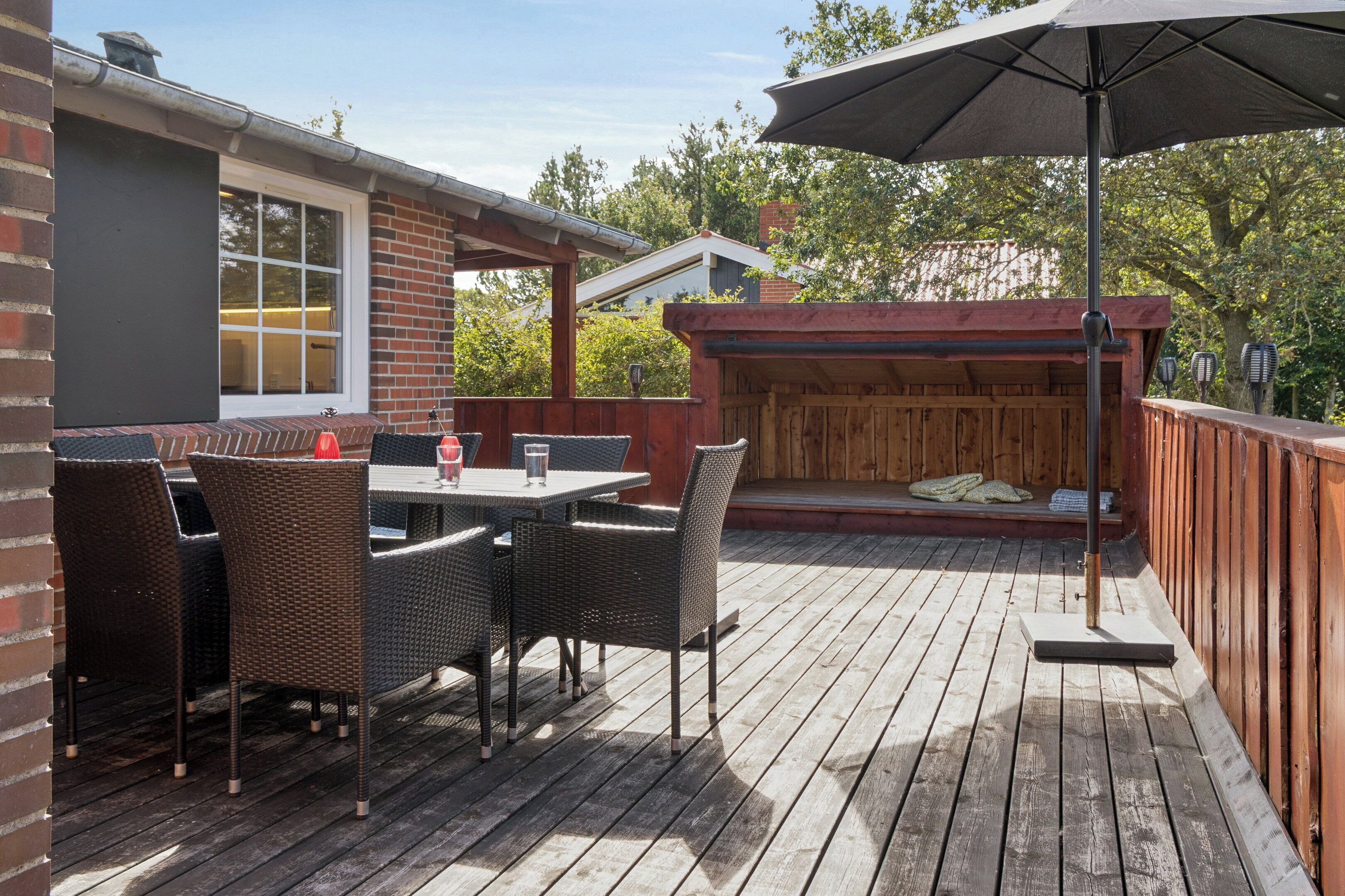 An outdoor patio with a wooden deck, wicker furniture, and a covered seating area.