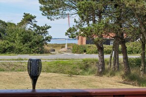 A view from a window overlooking a road with a body of water in the distance, trees, and a building with a red roof.