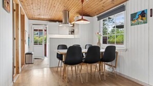 Un coin repas avec une table et des chaises en bois, un luminaire suspendu et une vue sur la verdure à l’extérieur.
