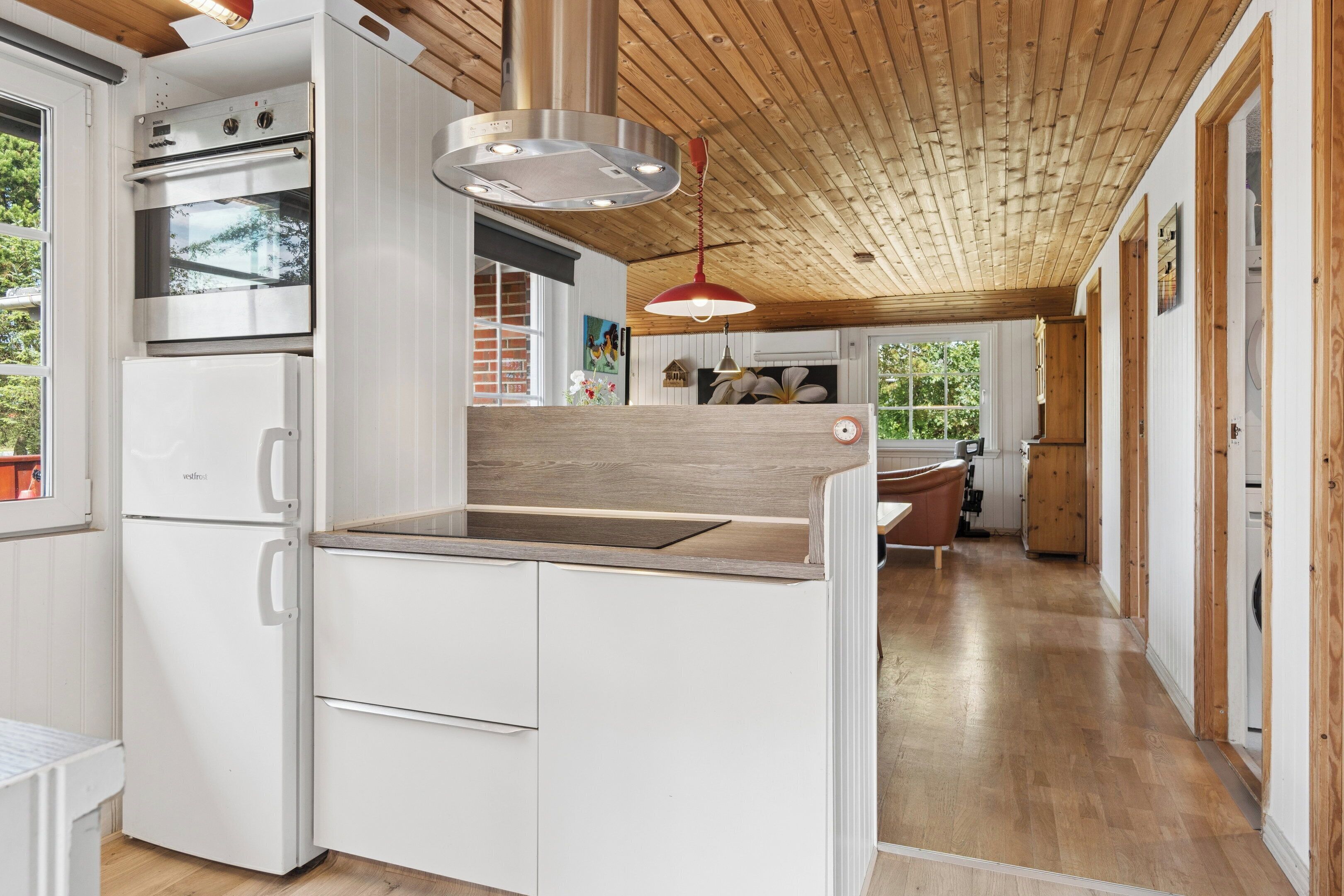 A modern kitchen with white cabinetry, a Bosch oven, and a wooden ceiling.