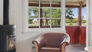 Une pièce avec un poêle à bois, un fauteuil en cuir et une fenêtre donnant sur un jardin.