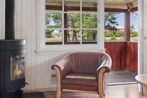 Une pièce avec un poêle à bois, un fauteuil en cuir et une fenêtre donnant sur un jardin.