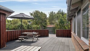 A wooden deck with picnic tables and an umbrella, surrounded by a wooden fence and trees.