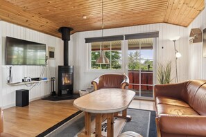 A cozy living room with a fireplace, wooden ceiling, and a large window.
