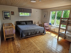 Une chambre à coucher avec un lit, un berceau, un bureau et une fenêtre donnant sur un paysage verdoyant.