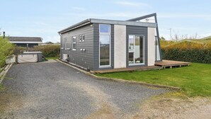 Ein modernes, eingeschossiges Haus mit Kiesauffahrt, kleiner Terrasse und gepflegtem Rasen.