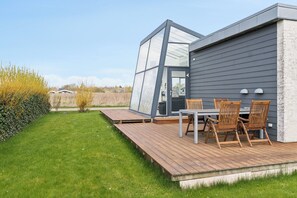 A modern house with a deck, a glass-enclosed room, and a dining area with chairs. - Modern summer house with fantastic skylight (Slagelse)