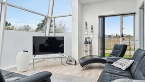 Ein modernes Wohnzimmer mit großem Fernseher, Ledersofa und Glastür zum Garten.
