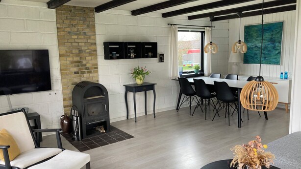 A modern living room with a fireplace, dining area, and a large TV mounted on the wall. - Cozy cottage close to the beach. (Bogense)