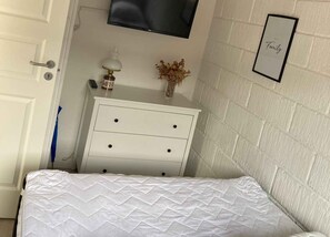 A bedroom with a bed, a white dresser, a TV mounted on the wall, and a framed 'Family' sign. - Cozy cottage close to the beach (Bogense)