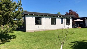 A single-story building with a flat roof, a small porch area, and a well-maintained lawn. - Cozy cottage close to the beach. (Bogense)