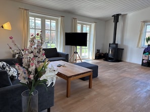Uma sala de estar com sofá, mesa de centro, televisão, lareira e grandes janelas.