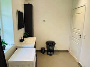A bathroom with a white sink, a mirror, a black cabinet, a trash bin, and a white door.