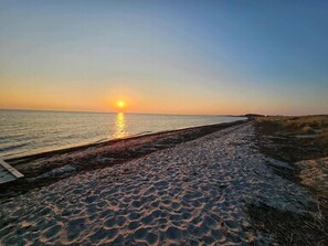 A beach with a wooden walkway leading to the water, a sunset in the background, and a clear sky.