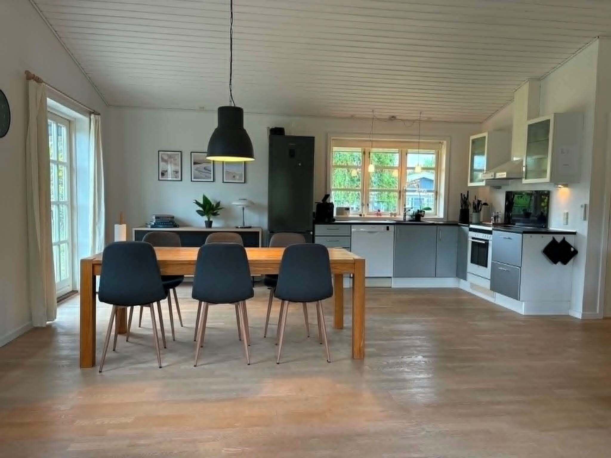 A modern kitchen with a dining area, wooden flooring, and a large window.