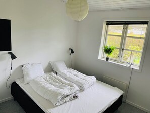 A bedroom with a bed, two bedside lamps, a window with a view, and a hanging light fixture.