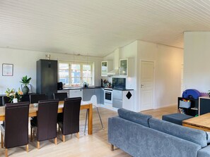 A modern kitchen with a dining area, a grey sofa, and a wooden table. - Lovely cottage with secluded garden (Rødby)