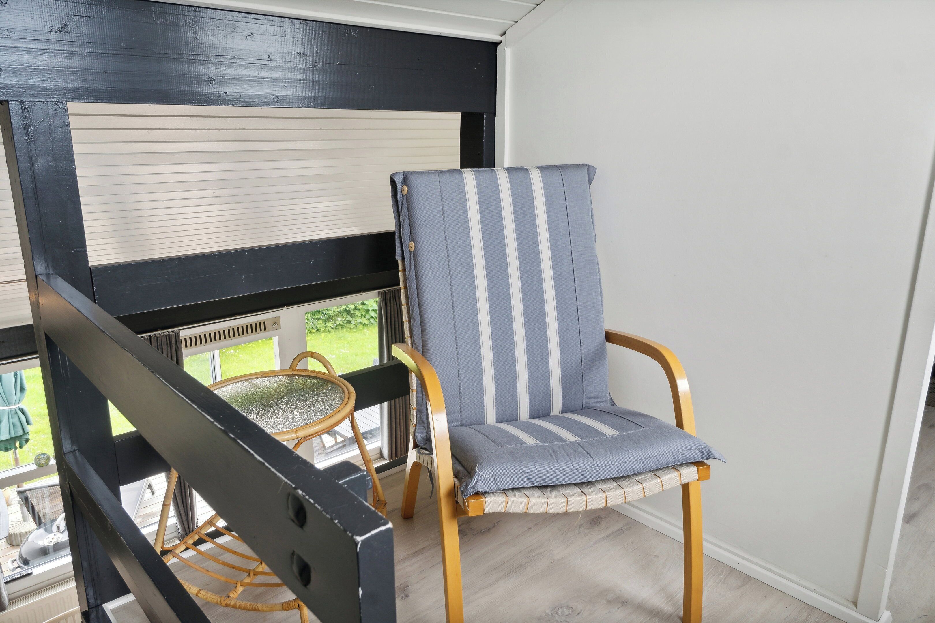 Une pièce avec une fenêtre à cadre noir, une chaise en osier et un fauteuil à rayures.