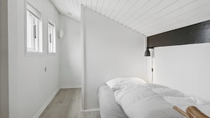 A bedroom with a bed, a wooden chair, a white wall, and a window.