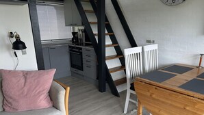 A loft-style room with a dining table, a sofa, a staircase, and a kitchen area.
