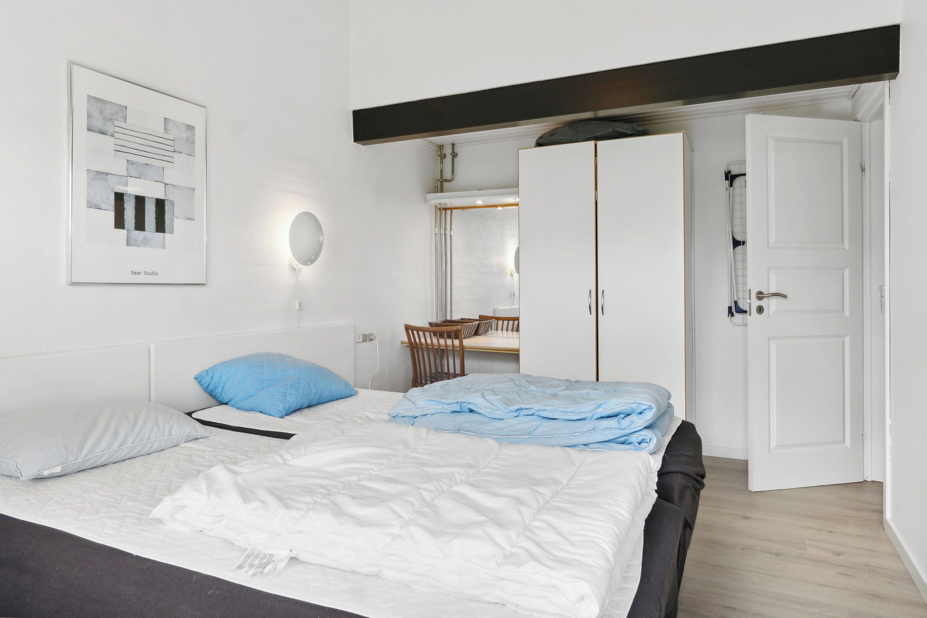 Une chambre à coucher avec un lit, un bureau, une chaise, une armoire et un tableau encadré au mur.