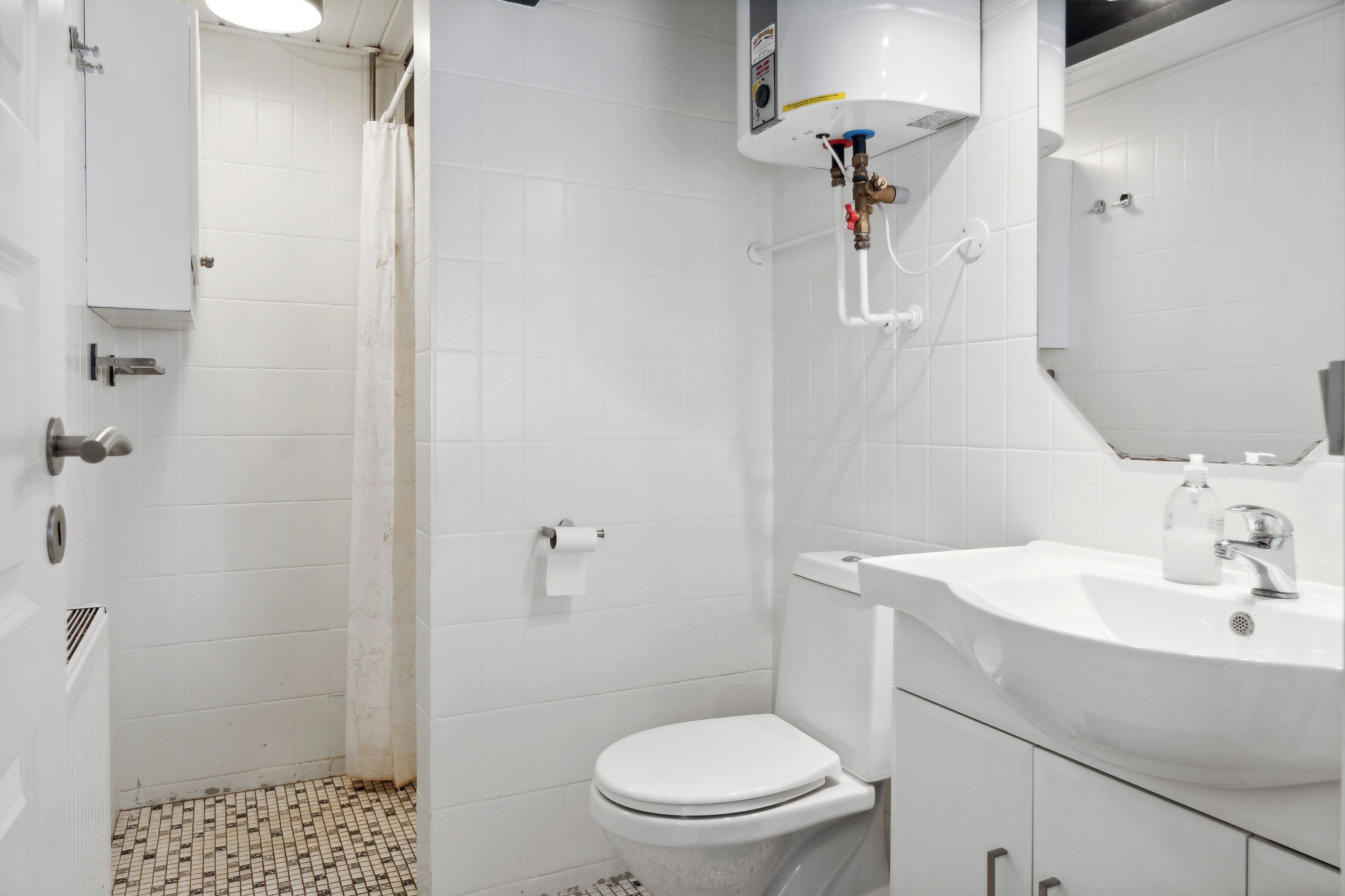 Une salle de bain comprenant des toilettes, un lavabo, une douche et des murs carrelés.