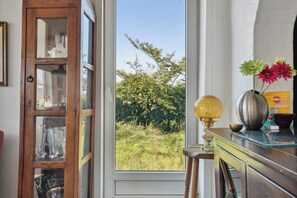 A room with a large window, a wooden cabinet with glass doors, and a table with a lamp and decorative items.