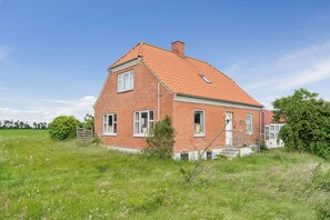 A red brick house with a sloped roof, a small porch, and a grassy yard.
