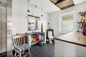 Ein Badezimmer mit Holzstuhl, Waschbecken, Toilette und einem Fenster mit Blick auf Bäume.