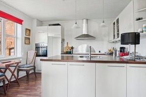 A modern kitchen with white cabinets, a wooden countertop, a stainless steel range hood, and a window with a red awning.