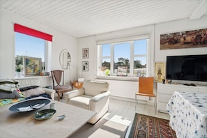 A room with a sofa, a dining table, a TV, and a window with a view.