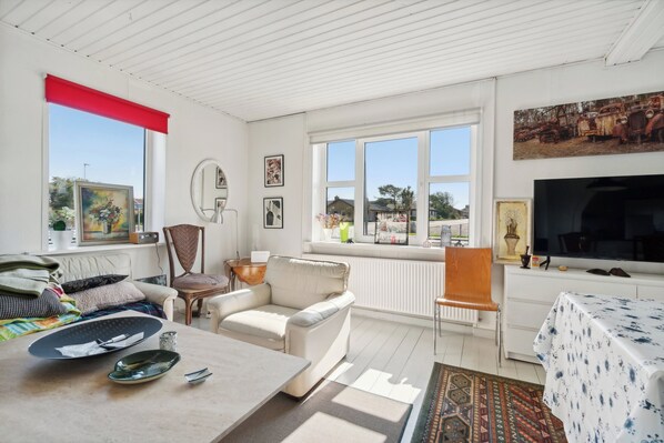 A room with a sofa, a dining table, a TV, and a window with a view.