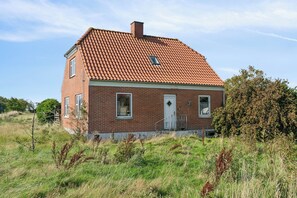 Ein einstöckiges Haus aus Ziegeln mit rotem Ziegeldach, einer Haustür und einem kleinen Fenster.