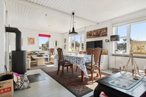 A dining area with a table set for four, surrounded by chairs, a black stove, and a large window with a view.