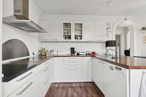 A modern kitchen with white cabinets, a stainless steel range hood, and a wooden countertop.