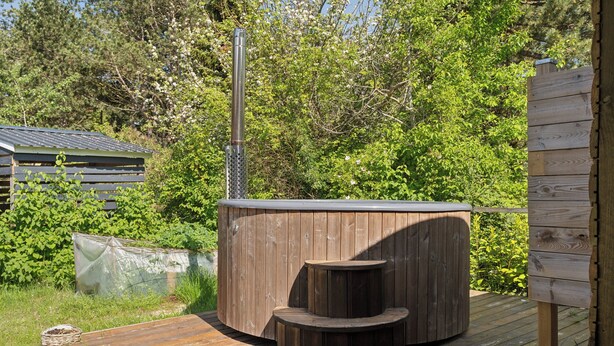 A hot tub on a wooden deck with a wooden structure in the background. - Cozy house with outdoor spa. (Væggerløse)