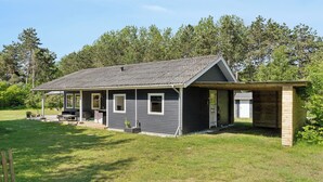 A single-story house with a covered porch, a small attached garage, and a well-maintained lawn. - Cozy house with outdoor spa. (Væggerløse)