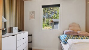 A bedroom with a bed, a dresser, a window with a view of trees, and a sign on the wall. - Cozy house with outdoor spa. (Væggerløse)