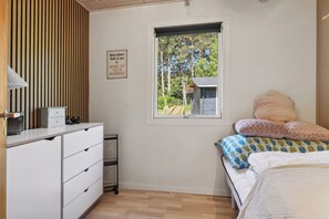 A bedroom with a bed, a dresser, a window with a view of trees, and a sign on the wall. - Cozy house with outdoor spa (Væggerløse)