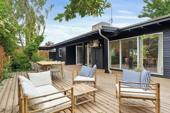 Eine Holzterrasse mit Gartenmöbeln, darunter eine Couch und Stühle sowie ein Esstisch.