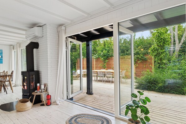 A modern interior with a large sliding glass door leading to an outdoor deck, a built-in wood stove, and a cozy seating area.