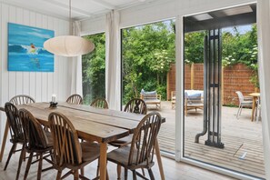 A wooden dining table with chairs, a painting, and a view of a wooden deck and garden.