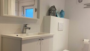 A bathroom with a white sink, mirror, toilet, and decorative items on the wall. - Holiday Cottage in Harbor Town of the Year (Allinge)