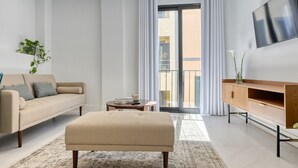 A modern living room with a sofa, ottoman, and a TV on a wooden cabinet. - Beco Santa Emilia 2I, a Home in Madeira (Funchal)