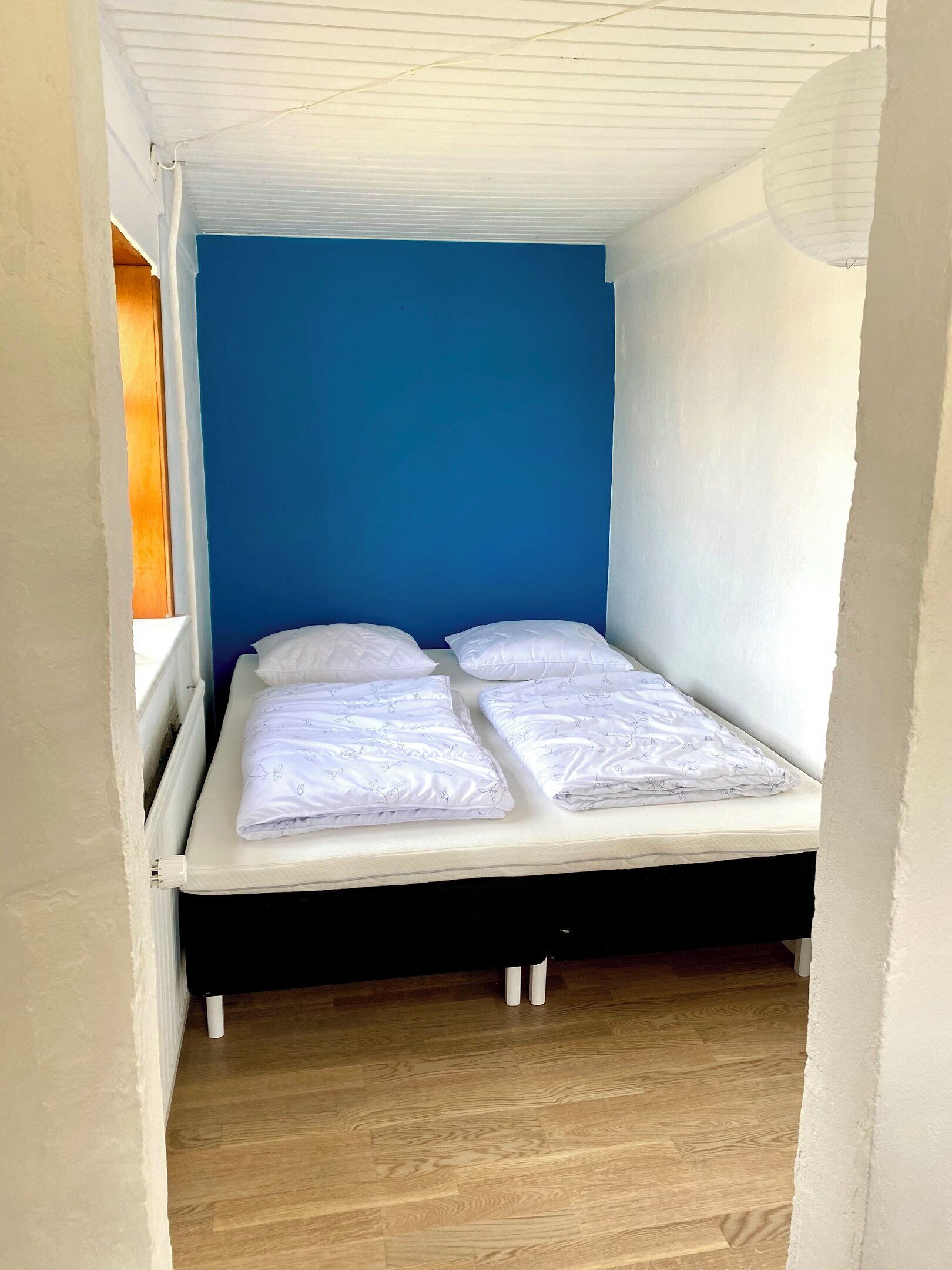 Una stanza piccola e stretta con un letto singolo, una parete blu e un pavimento di legno.