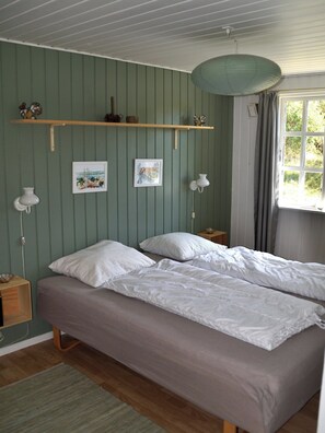 A room with a bed, two wall-mounted lamps, a window with curtains, and two framed pictures on the wall.