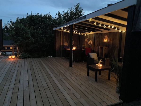 A wooden deck with string lights, a covered seating area, and a view of trees.