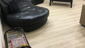 En stue med en sort lædersofa, et fjernsyn på et stativ, et lille bord og en lyserød legetøjsvogn.