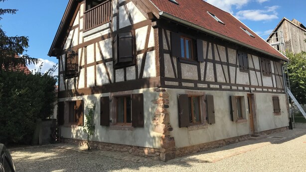 Et traditionelt bindingsværkshus med skråt tag, flere vinduer og en lille balkon.